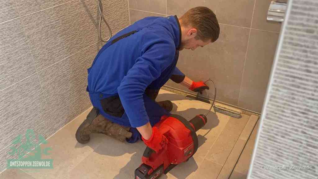 Een monteur ontstopt een langwerpige douchegoot met een elektrische veer, een doucheputje verstopt door haren en zeep in Zeewolde