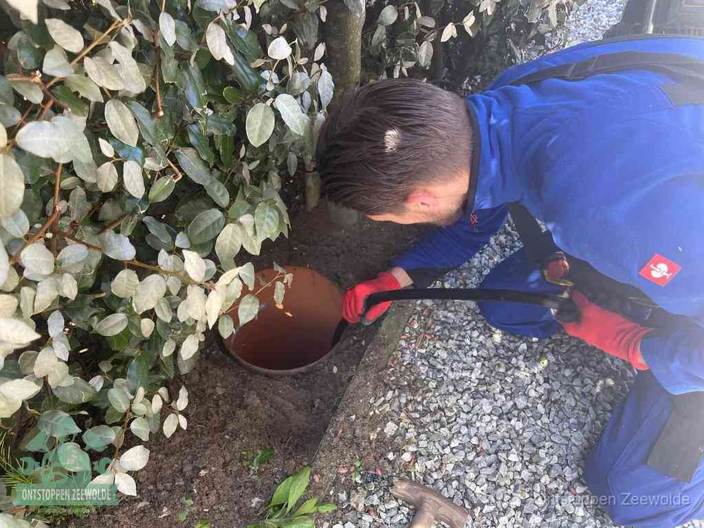 Een monteur voert een slang in een geopende rioolput in de tuin om het hoofdriool te ontstoppen in Zeewolde
